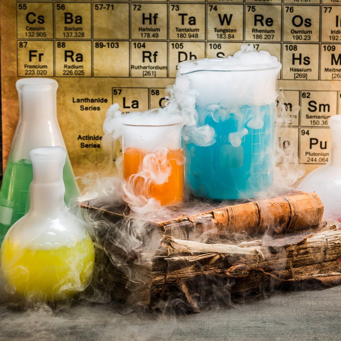 Colorful chemical beakers with fog spilling out, placed in front of a periodic table — symbolizing artificial or synthetic ingredients in skincare or cosmetics.