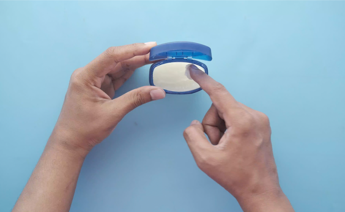 Hands holding petroleum jelly jar, finger dipping into petroleum jelly.